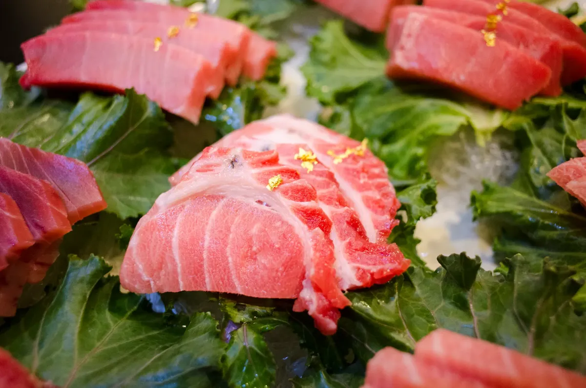 A close-up of fresh tuna sashimi elegantly presented on leafy greens, garnished with gold flakes.