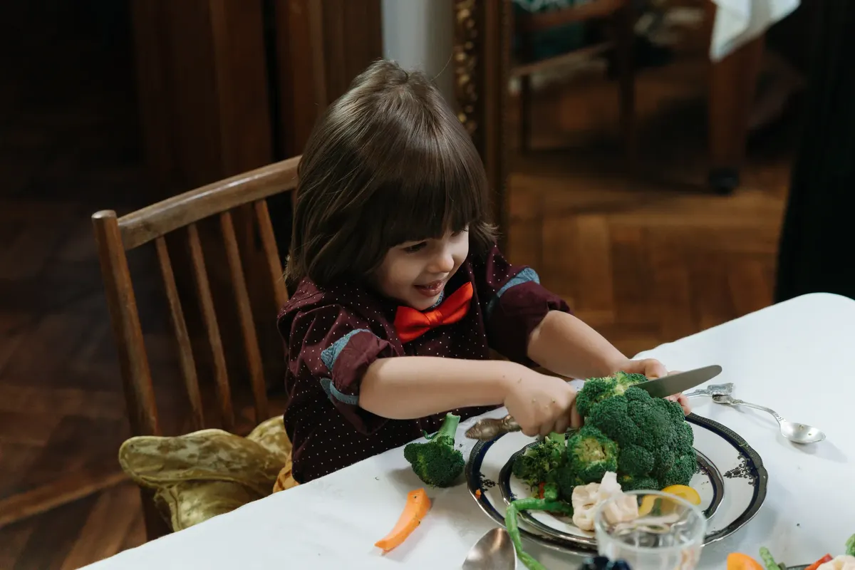Young child excitedly cutting broccoli during a healthy meal at home.