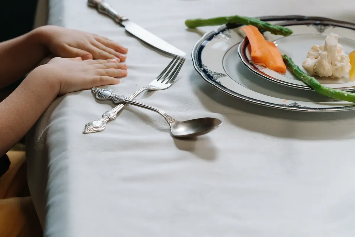 A child's hands at a dining table with plates of vegetables, showcasing a healthy meal.