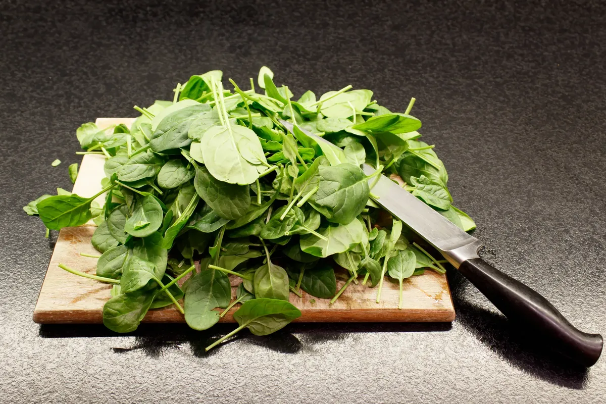 A pile of fresh spinach leaves on a wooden cutting board with a knife nearby.