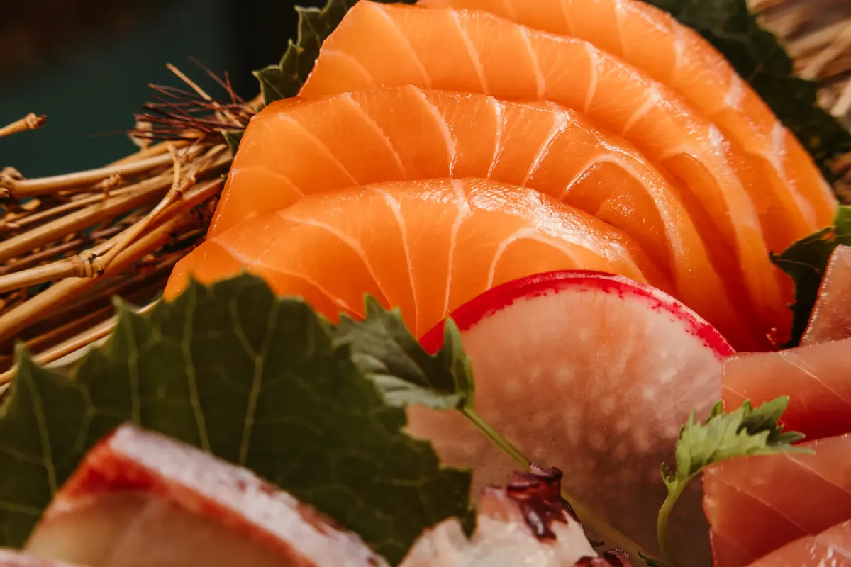 A close-up view of fresh salmon sashimi garnished with radish slices and leaves, showcasing Japanese culinary art.